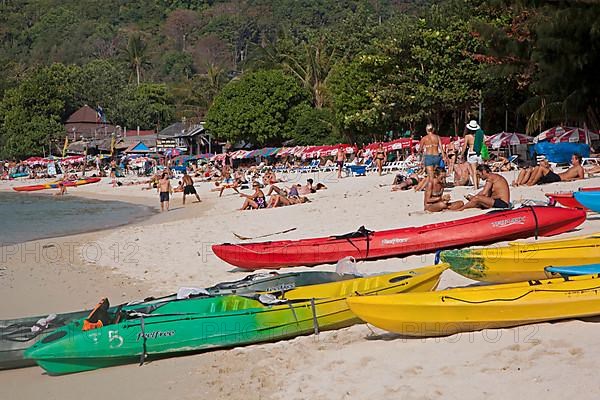 Colourful canoes and western tourists sunbathing on the beach of one of the Ko Phi Phi islands