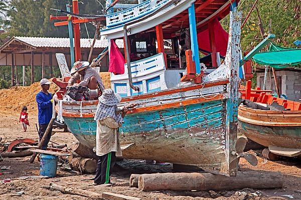 Boat builders renovating a traditional Thai wooden fishing boat on the beach in southern Thailand