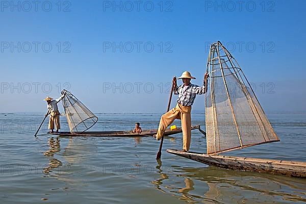 Two Intha fishermen steer traditional fishing boats by wrapping their leg around the oar