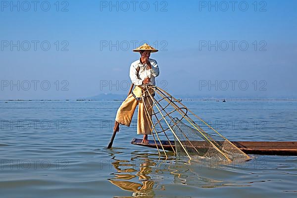 Intha fisherman steering traditional fishing boat by wrapping his leg around the oar