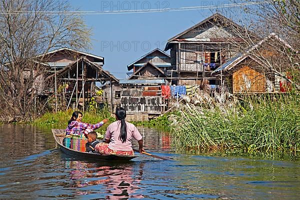 Intha woman with child in proa row to lake village with traditional wooden houses on stilts in Inle Lake