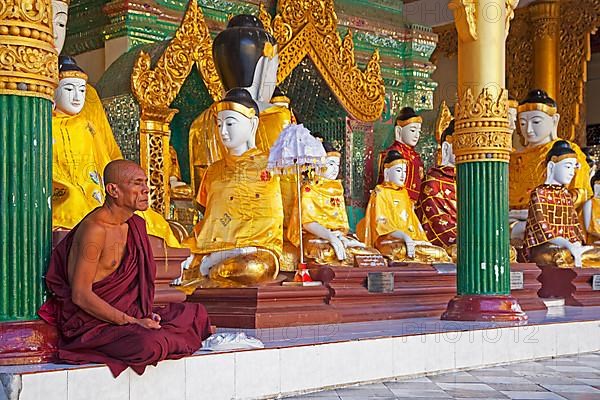 Buddhist monk praying in front of Buddha statues at the Shwedagon Zedi Daw Pagoda in Yangon