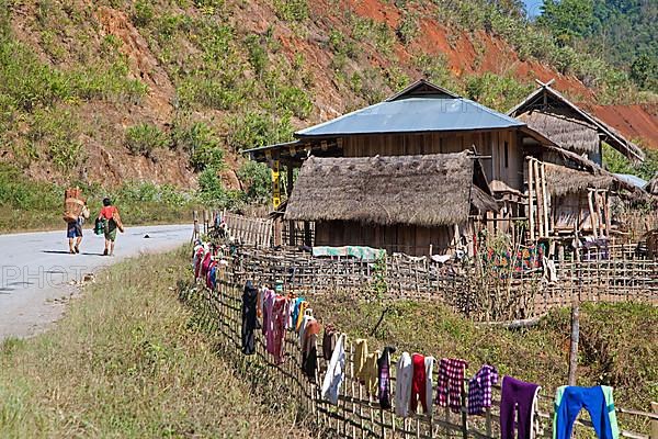 A Burmese man carries firewood on his back and laundry drying in the sun along the fence in a rural village in Tachileik District