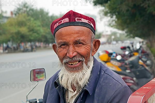 Close-up of an elderly Uighur man with a beard wearing a doppa in Qiemo