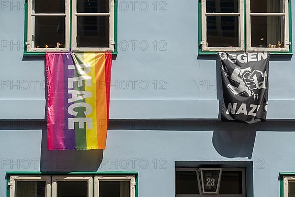 A rainbow-coloured peace flag and a black flag with the inscription Against Nazis hang from windows of a residential building in the old town