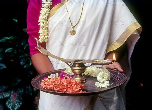 A girl holding oil lamp and flowers on a tray during Onam festival