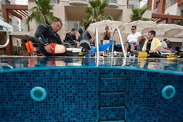 Disabled diver with prosthetic legs and instructor at edge of swimming pool