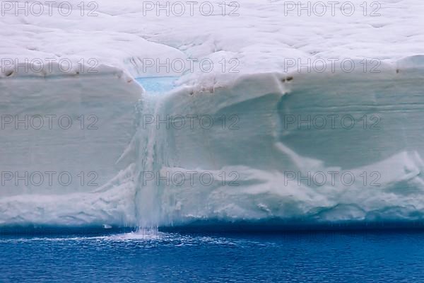 Meltwater flowing from the ice wall of the melting Brasvellbreen Glacier into the Arctic Ocean