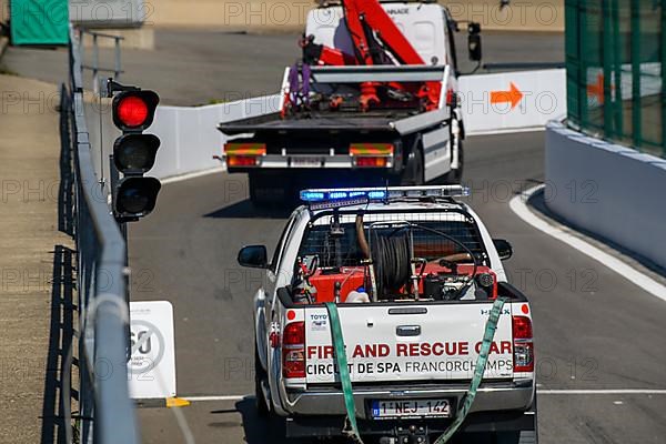 Tow truck and rescue vehicle drive through exit from pit lane onto race track at red lights due to race stoppage