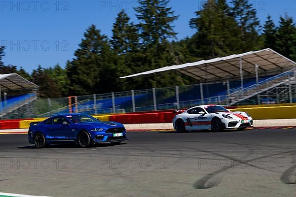 Ford Mustang Porsche Cayman GT4 races at full throttle at exit of corner hairpin La Source of racetrack