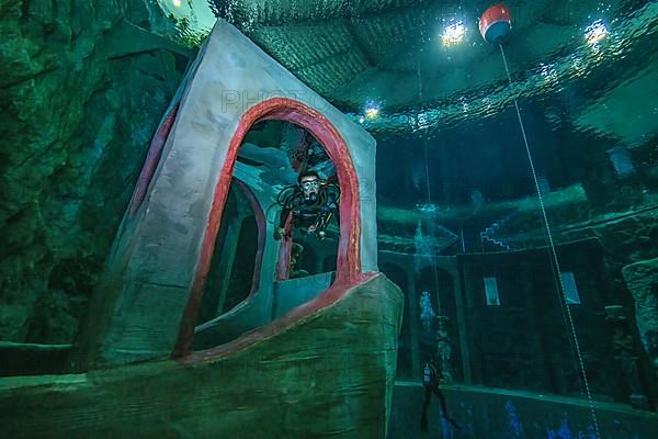Female diver dives in 10 metres depth in indoor diving tower through imitated bridge house over bow of stylised small ship