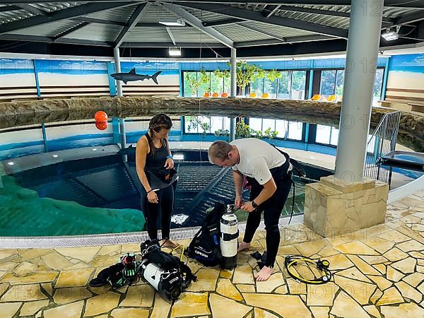 Pair of divers prepare dive equipment for dive in indoor diving tower