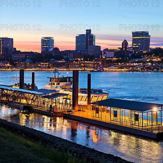 Pier for the harbour ferries at the Stage Theater on the Elbe in the evening in front of the city skyline