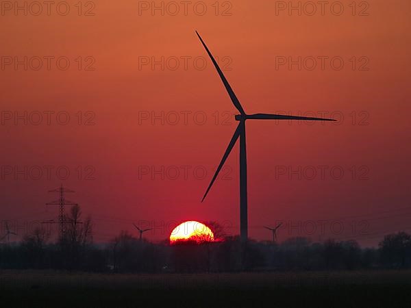 Wind turbines and power lines in front of the setting sun in Hamburg's Vier- und Marschlanden. Ochsenwerder