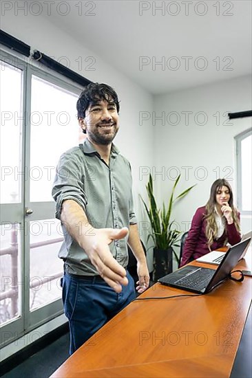 Businessman in office meeting room stands up and extends hand to greet someone out of frame. Concept of welcome