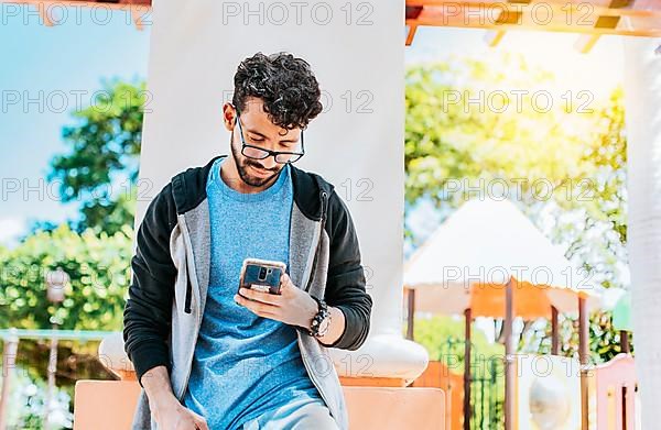 Smiling handsome man using a phone leaning on a wall in a park