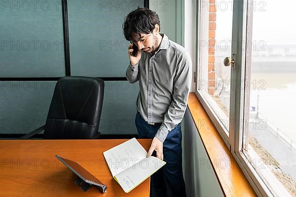 Latino businessman working in an office overlooking the river. Talking on the phone and reviewing notes