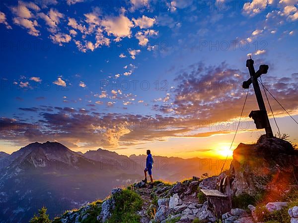 Mountaineer standing at sunset at the summit cross of the Brettgabel