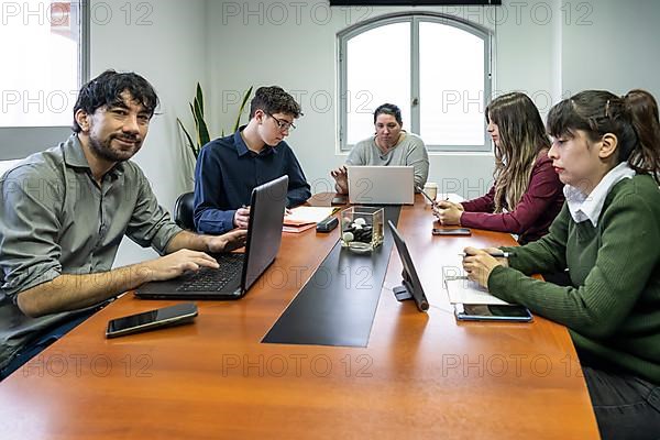 Group of employees sitting around the office meeting table working on their notebooks