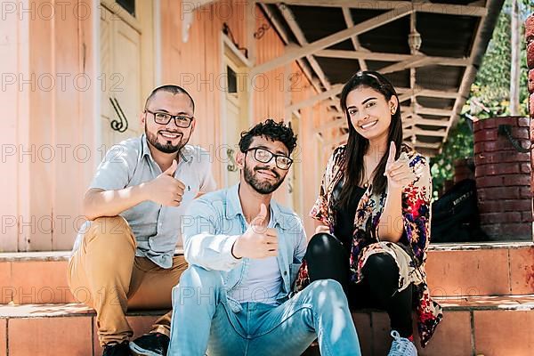 Group of happy friends sitting on the stairs giving thumbs up. Portrait of happy teenagers sitting outside giving thumbs up