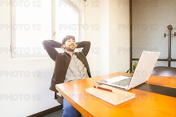 Businessman sitting at the head of the meeting table with his hands behind his head