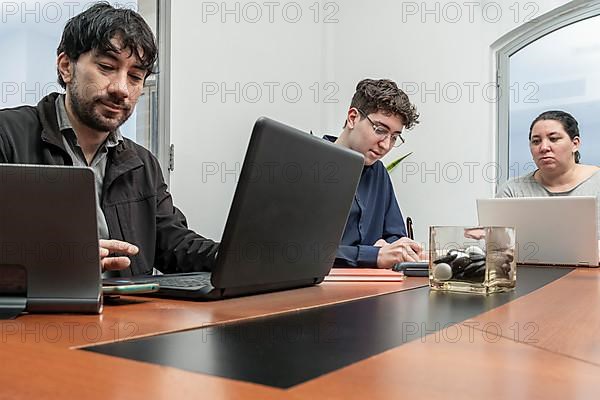 Group of employees sitting around the office meeting table working on their notebooks