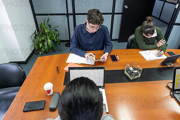 Group of employees sitting around the office meeting table working on their laptops and note pads