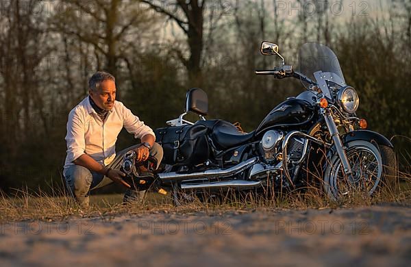 Man squatting on beach next to motorbike