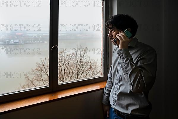 Latino businessman working in an office overlooking the river. Talking on the phone while he looks out the window
