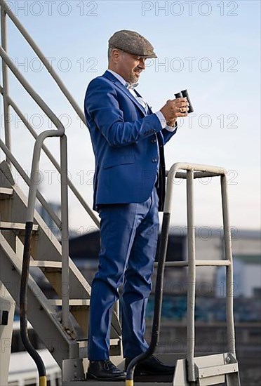 Man with blue suit and hat has binoculars in his hand
