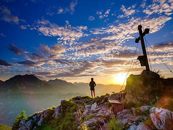 Mountaineer standing at sunset at the summit cross of the Brettgabel