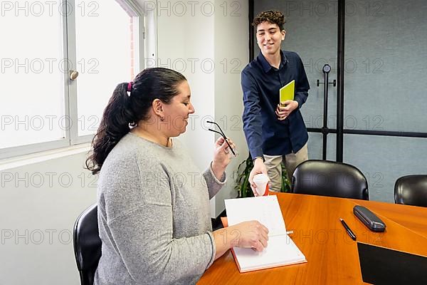 Assistant serving coffee to businesswoman sitting at head of meeting table