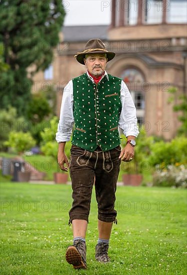 Man in Bavarian traditional costume with hat walking across lawn