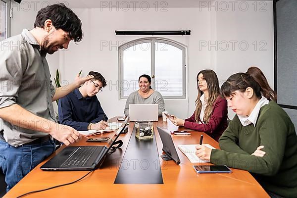 Group of employees sitting around the office meeting table working on their notebooks