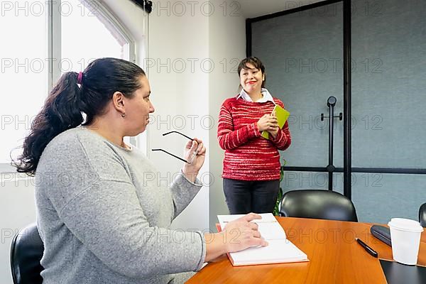Businesswoman sitting at the head of the meeting table looking at her assistant standing next to her