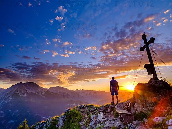 Mountaineer standing at sunset at the summit cross of the Brettgabel