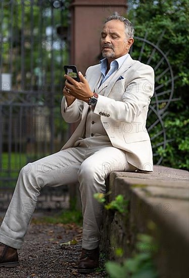 Man in suit sitting on a wall and looking strained into his phone
