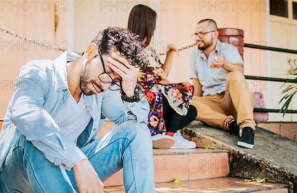 Sad man seeing his girlfriend cheating with his friend. Sad boyfriend sitting on some stairs while his girlfriend talking to another man. Girl talking to another man and her boyfriend is offended