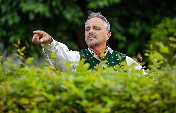 Neighbour in Bavarian traditional traditional costume points with hand over hedge