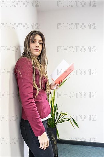 Young blonde businesswoman standing in the meeting room holding her note pad and looking at the camera