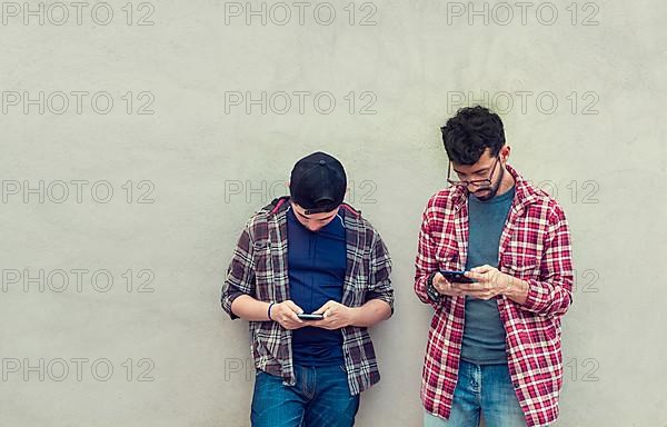 Two teenage friends on a wall checking their cell phones
