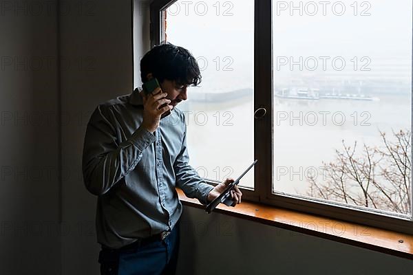 Latino businessman working in an office overlooking the river. Talking on the phone and reviewing notes