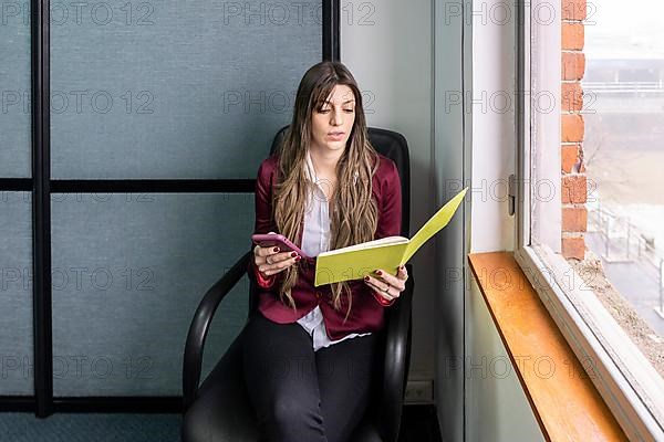 Young blonde business woman sitting in her office using the phone while checking notes