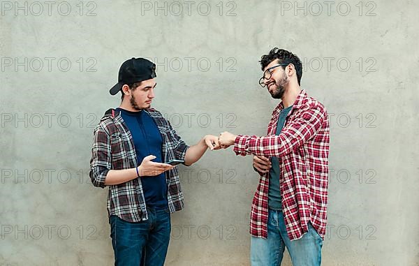 Two teenage friends greeting each other by fist bumping outdoors. Two smiling young guys bumping fists near a wall. Concept of two smiling friends bumping fists friendly