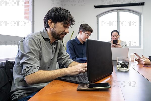 Group of employees sitting around the office meeting table working on their notebooks