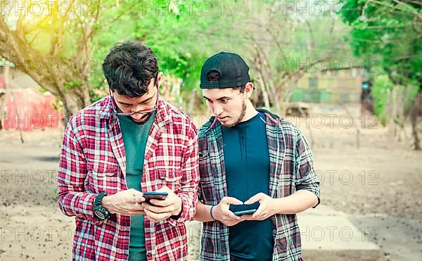 Jealous friend spying on his friend's cellphone outdoors