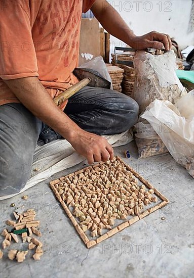 Moroccan cellular craftsman at work: hammering small pieces out of a tile