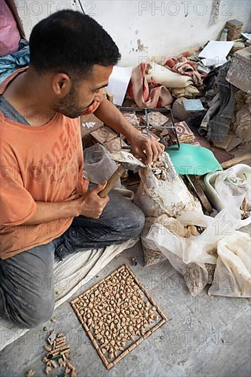 Moroccan cellular craftsman at work: hammering small pieces out of a tile