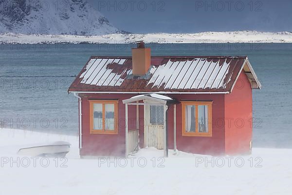 Red insulated wooden hut along the coast in the snow in winter