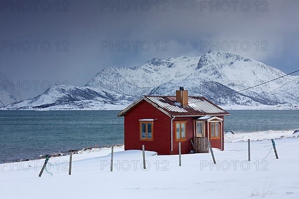 Red insulated wooden hut along the coast in the snow in winter
